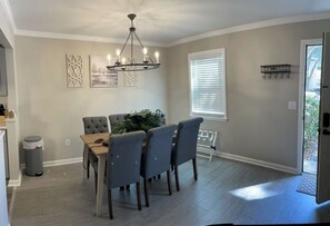 A dining area with a table and chairs, a chandelier, and a window with blinds.