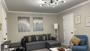 Ein modernes Wohnzimmer mit einem grauen Ecksofa, einem blauen Sessel, einem kleinen Tisch mit einer Vase und einem Schreibtisch mit Stuhl.