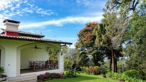Una casa con un patio, escalones que conducen a la entrada y un jardín con diversas plantas y un árbol con flores rojas.