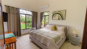 A bedroom with a bed, a bedside table, a lamp, and a view of a garden through the window.