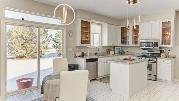 A modern kitchen with white cabinets, a central island, stainless steel appliances, and a large sliding glass door leading to a patio. - Cozy Comfort/ 2-Bedroom Plainfield Getaway (Plainfield)