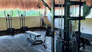 A gym with a thatched roof, exercise equipment, and a bench.