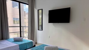 A hotel room with two beds, a TV mounted on the wall, and a window with curtains.
