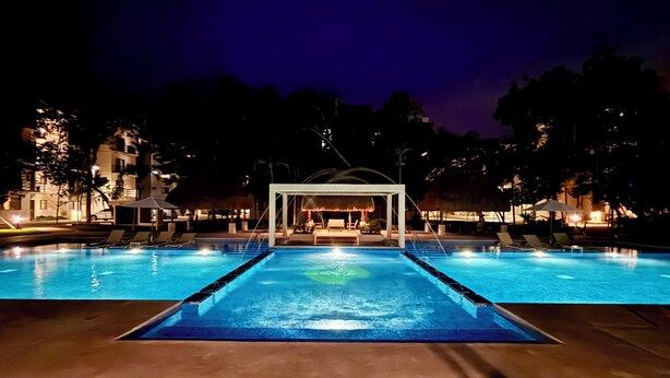 A nighttime swimming pool with lounge chairs and a covered seating area.