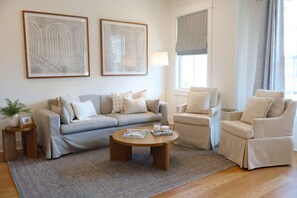 Una sala de estar con un sofá, un sillón, una mesa de centro, una lámpara y dos cuadros en la pared.
