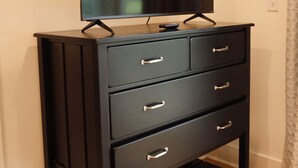 A black TV stand with a flat-screen TV, three drawers, and a remote control. - 121 Allison Way townhouse (Algood)