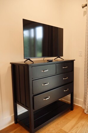 Un mueble negro para televisor con televisor de pantalla plana, tres cajones y un control remoto.