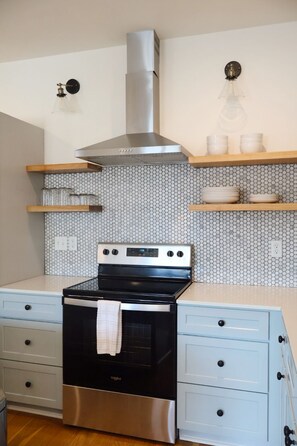 Una cocina con estufa de acero inoxidable, horno negro, armarios azul claro y un salpicadero con motivo hexagonal, además de una campana extractora de acero inoxidable.