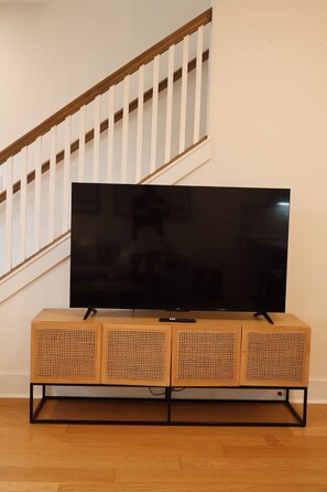 Un televisor de pantalla plana sobre un mueble de madera, con una escalera al fondo.