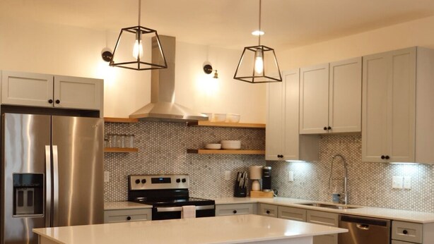 Una cocina moderna con una isla central, electrodomésticos de acero inoxidable e iluminación colgante.