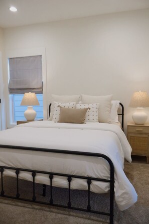 A neatly made bed with a metal frame, two bedside lamps, and a window with a blind. - 121 Allison Way townhouse (Algood)