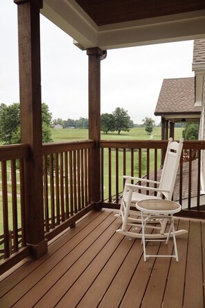 A wooden deck with a covered porch, two white rocking chairs, and a view of a green landscape. - 121 Allison Way townhouse (Algood)
