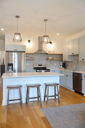 A modern kitchen with a central island, bar stools, stainless steel appliances, and pendant lighting.