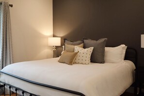 A bed with a headboard, a bedside lamp, and a window with curtains.