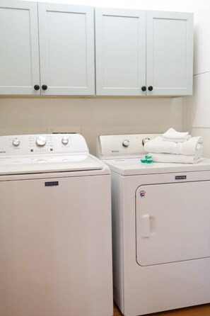 Zona de lavandería con dos lavadoras Maytag y una secadora, armarios blancos arriba y una toalla doblada sobre la secadora.