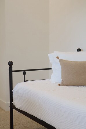 Una cama con colchón blanco, almohada marrón y estructura metálica negra, con una pared lisa al fondo.