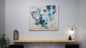 Un intérieur moderne avec un bureau en bois, deux chaises noires, un tableau abstrait accroché au mur, une lampe sur pied et une plante en pot.
