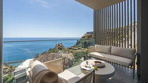 Un balcón con sofá y una mesa redonda, con vistas a la costa, edificios y acantilados.