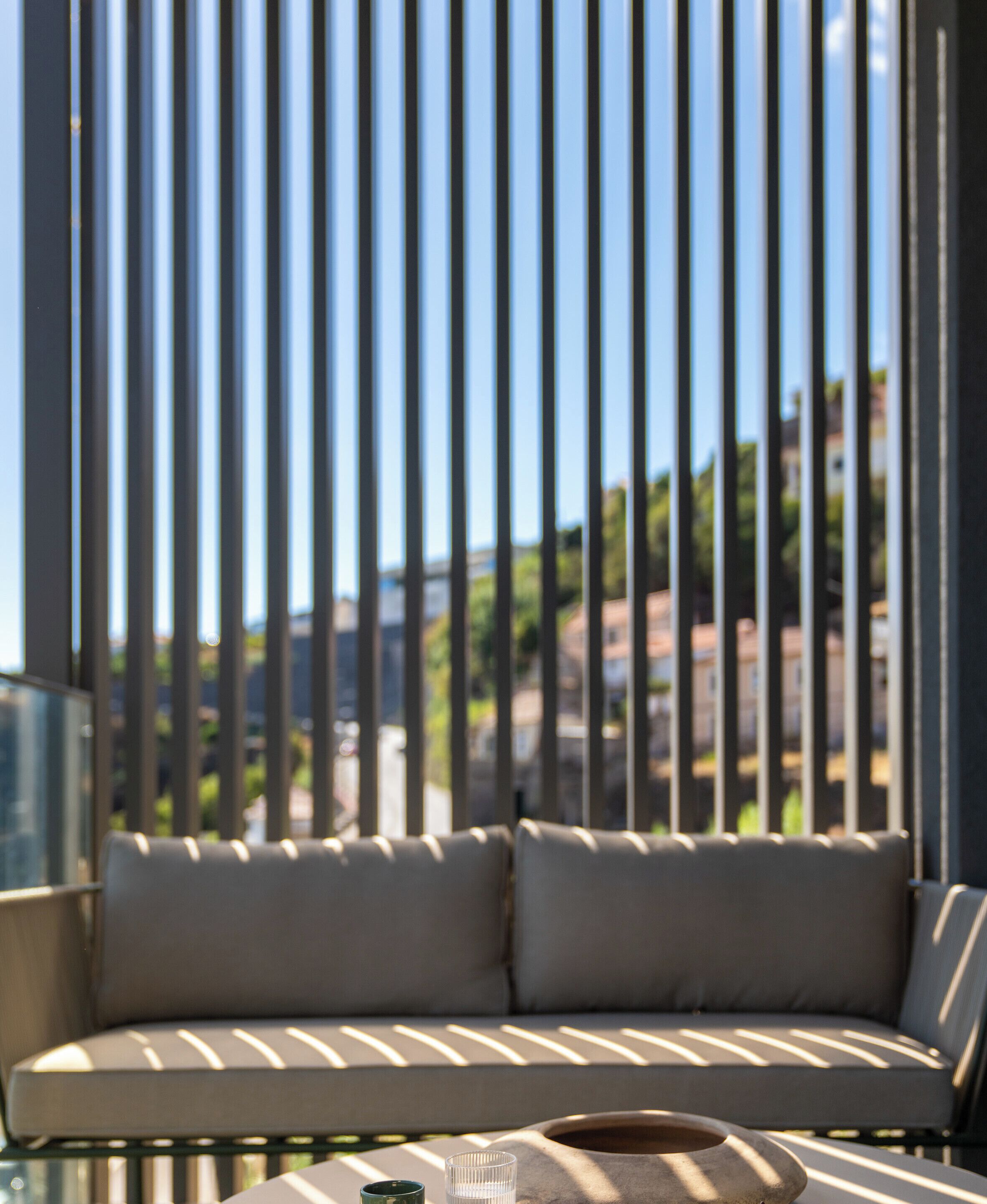 Een zonnig terras met zitgedeelte, een bank en een tafel, met zicht door verticale zonwering.
