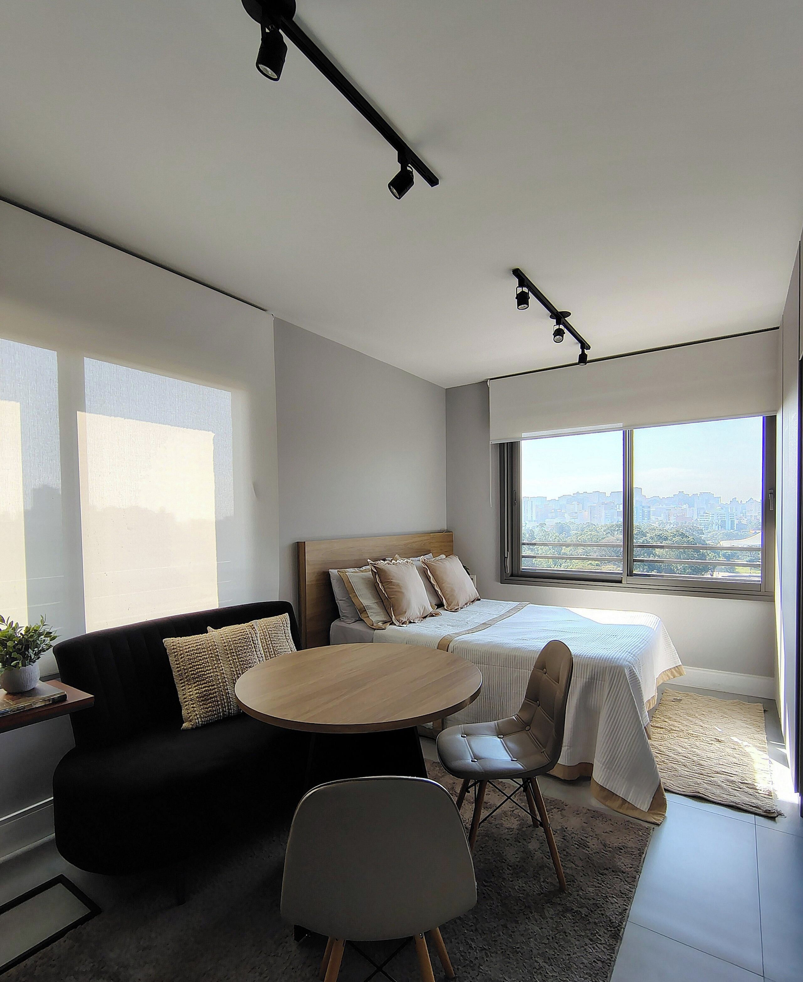 Une chambre d’hôtel moderne, équipée d’un lit, d’un canapé, d’une table à manger et d’une chaise. Une grande fenêtre offre une vue sur la ville.