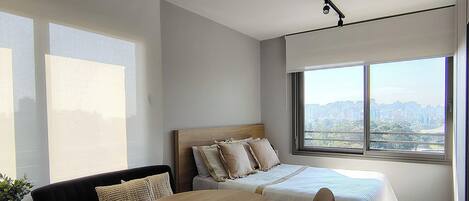 Une chambre d’hôtel moderne, équipée d’un lit, d’un canapé, d’une table à manger et d’une chaise. Une grande fenêtre offre une vue sur la ville.