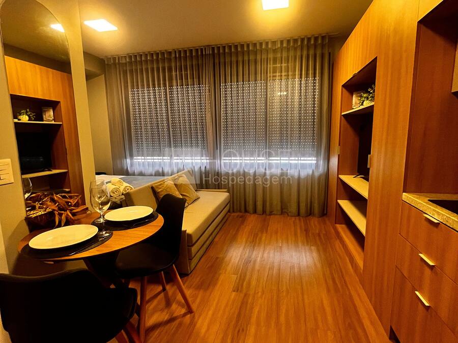 Ein kleines Hotelzimmer mit Essbereich, einer Couch, einem Fenster mit Vorhängen und Holzmöbeln.