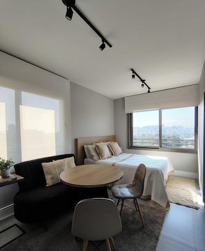 Ein modernes Hotelzimmer mit Bett, rundem Tisch, einer Sitzecke und Blick auf die Stadt.