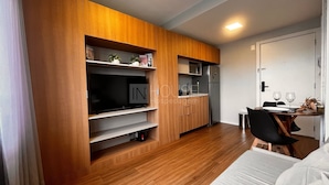 A modern kitchen with wooden cabinetry, a built-in TV, and a dining area with a table and chairs. - Jp redenção  (Porto Alegre)