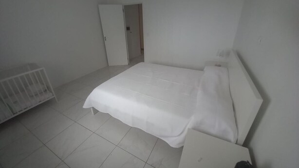 A small, sparsely furnished room with a single bed, a white radiator, and a door leading to another room. - Casa Titanic - Sea view! Ribeira da Prata (Praia)
