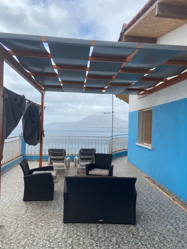 Un espace extérieur aménagé, abrité et doté de chaises et d’une table, offrant une vue sur un plan d’eau et une montagne.