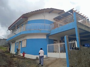 Un bâtiment à deux étages, à la façade bleue et blanche, doté d’un balcon à l’étage supérieur et d’une entrée fermée par un portail.