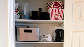Een keukenkast met planken vol pannen, braadpannen, een koffiezetapparaat en een bak voor popcorn.