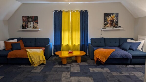 Una sala de estar acogedora con dos sofás azul oscuro, una cortina amarilla y azul, y una mesita con un cuenco rojo.