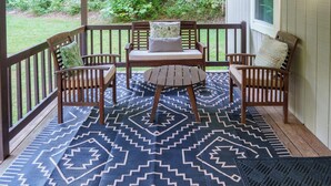 Une véranda couverte avec un banc et une table en bois, des tapis à motifs et une vue sur un paysage verdoyant.