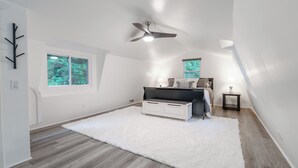 Une chambre à coucher avec un lit, un ventilateur de plafond, une fenêtre et un tapis blanc.
