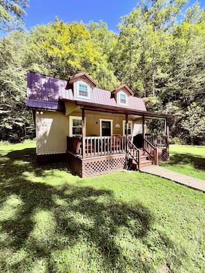 Une cabane en bois à deux étages, dotée d’un porche et entourée d’une végétation luxuriante.