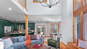 A spacious living room with a sofa, ottoman, and a dining area in the background. - Helen Haus: Golf Sim & Hot Tub Theater Retreat (Helen)