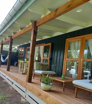 A covered outdoor area with wooden beams, a hammock, a table with chairs, and a potted plant. - Amori Villa & Cabin (Rarotonga)