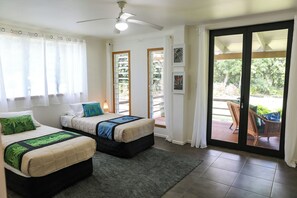 A hotel room with two beds, a ceiling fan, a large sliding glass door to a patio, and a view of greenery outside. - Amori Villa & Cabin (Rarotonga)