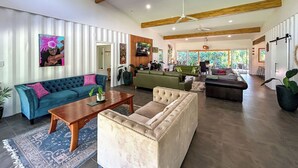 A spacious living room with a large sofa, a coffee table, and a fireplace. There is a television mounted on the wall and a ceiling fan. - Amori Villa & Cabin (Rarotonga)