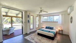 A bedroom with a bed, a ceiling fan, a window, and a door leading to a balcony. - Amori Villa & Cabin (Rarotonga)