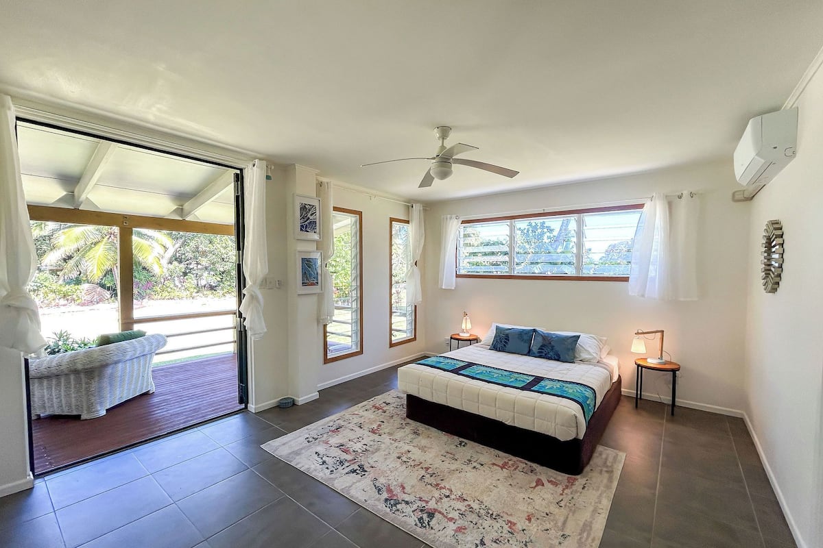 A bedroom with a bed, a ceiling fan, a window, and a door leading to a balcony.