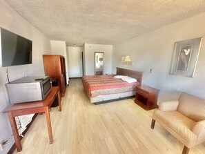 A hotel room with a bed, a desk with a television, a chair, and a wardrobe. - Albuquerque lnn   (Albuquerque)