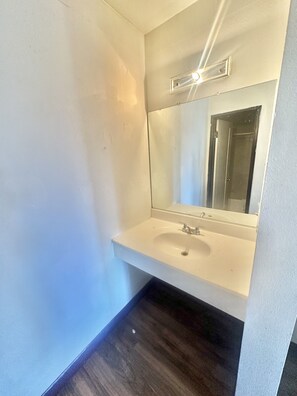 A bathroom with a white sink, a mirror, and a dark wooden floor. - Albuquerque lnn   (Albuquerque)