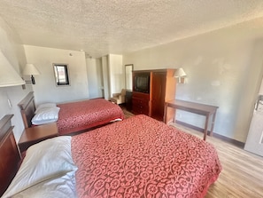 Quarto de hotel com duas camas, televisão, escrivaninha e espelho.