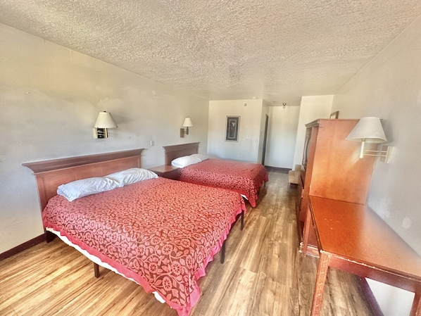 A room with two beds, wooden headboards, a wooden dresser, and two wall-mounted lamps.