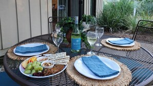 Una mesa redonda de metal con individuales tejidos, platos de comida y copas de vino blanco.