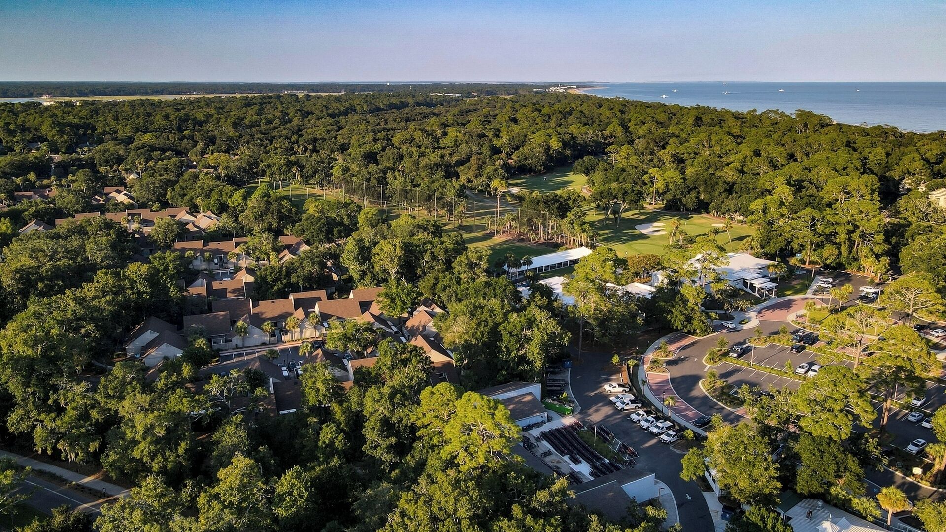 Luchtbeeld van een woongebied met huizen, een golfbaan en een waterlichaam in de verte.