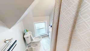 A small, compact bathroom with a toilet, a window, and a shower curtain.