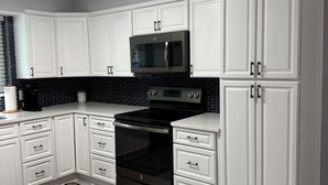 A modern kitchen with white cabinetry, a black stove, and a microwave. There is a sign above the cabinets indicating the address. - Gisella‘s Beach House II
Five minute drive to the beach (Vero Beach)